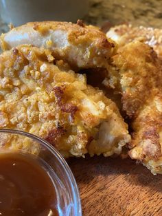 two fried chicken patties with dipping sauce on a wooden table next to a cup