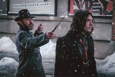 two people standing outside in the snow with one holding an umbrella and the other pointing at something