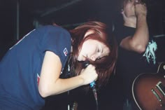 a woman with red hair is singing into a microphone while another man plays guitar behind her