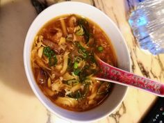 a bowl of soup with noodles and vegetables in it on a table next to a water bottle