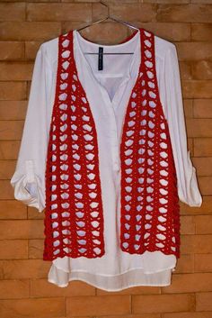 a red and white crocheted vest hanging on a brick wall