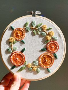 someone is holding up a small embroidery hoop with oranges and green leaves on it