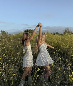 two young women in white dresses are standing in a field with yellow wildflowers