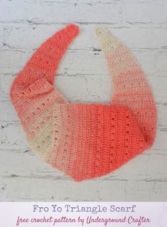 an orange and white crocheted scarf hanging on a brick wall with the text, pro yo triangle scarf free crochet pattern by underground crafter