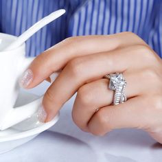 a close up of a person's hand with a ring on their finger, next to a cup and saucer