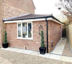 a small brick house with two plants in the front and one on the back side