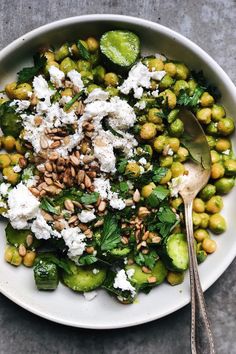 a white bowl filled with green vegetables and feta cheese on top of it next to two spoons