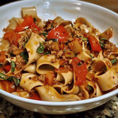 a white bowl filled with pasta covered in sauce and vegetables on top of a granite counter