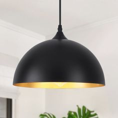 a black and gold pendant light hanging over a dining room table with potted plants