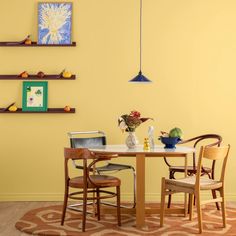 a dining room with yellow walls and chairs around a round table that has two vases on it