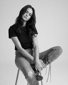 a woman sitting on top of a stool wearing ripped jeans and black t - shirt