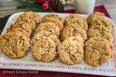 several cookies on a white plate next to a glass of milk and some pine cones