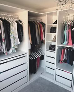 an organized closet with white drawers and clothes hanging from the ceiling, chandelier above