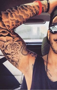 a man wearing sunglasses and a black tank top is sitting in a car with tattoos on his arm