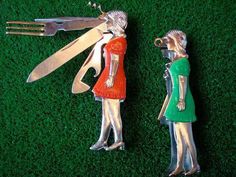 two metal figurines with scissors on top of green grass next to each other