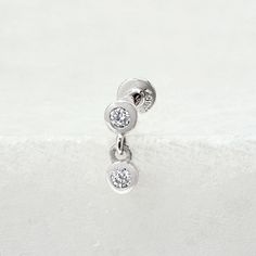 two round diamond earrings sitting on top of a white surface with the bottom bead down