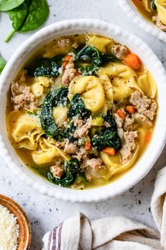 two bowls filled with pasta and spinach soup on top of a white countertop