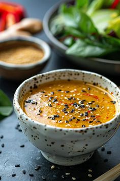 a white bowl filled with soup next to bowls of vegetables and seasoning on a table