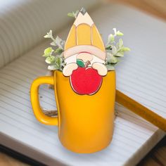 a yellow coffee mug with an apple on it and a paper clip sticking out of the cup