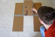 a young boy sitting on the floor next to some cardboard boxes and pointing at it