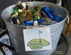 a metal bucket filled with lots of different types of beer and liquor bottles next to a sign that says the watering hole