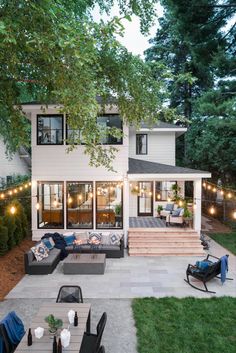 an outdoor patio with seating and string lights on the side of the house, surrounded by trees