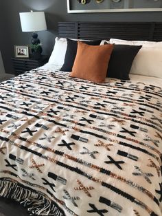 a bed with black, white and orange blankets on top of it next to a night stand