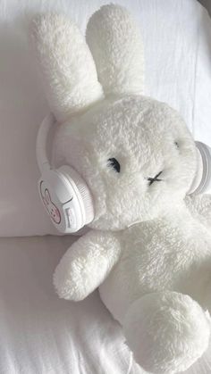 a white stuffed animal laying on top of a bed with headphones around it's ears