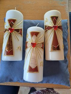 three white candles decorated with gold and red decorations on a blue pillow next to a wooden table