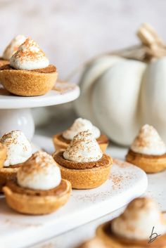 mini pumpkin pies with whipped cream on top are sitting on small white platters