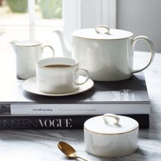 two white cups and saucers sitting on top of a book next to a spoon