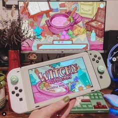 a person holding a nintendo wii game controller in front of a computer screen with an image of a witchy kitchen on it