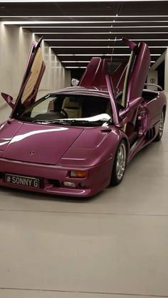 a purple sports car parked in a garage with its doors open and the hood up