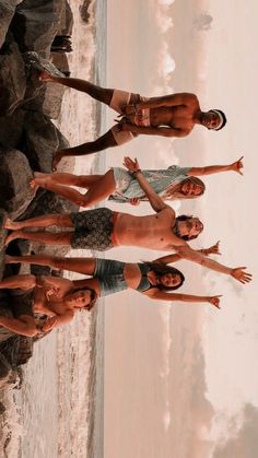 four young men standing next to each other on the beach with their arms in the air