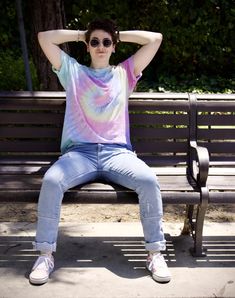 a woman sitting on a park bench with her hands behind her head and wearing sunglasses