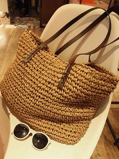 a straw bag sitting on top of a white chair next to sunglasses and a purse