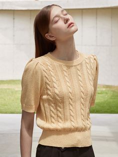 a woman with her eyes closed wearing a yellow sweater and black pants, standing in front of a building