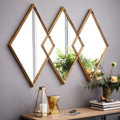 three mirrors are hanging on the wall above a table with books and flowers in vases