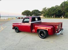 an old red pickup truck parked in a parking lot