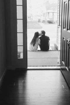 two people sitting on the floor in front of an open door and looking at each other