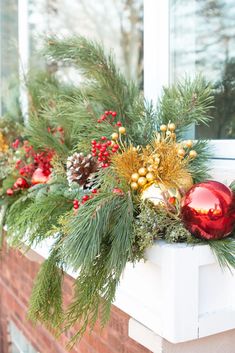 a window sill decorated with evergreen, pine cones and red baubs for christmas