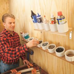 a man in plaid shirt holding paint cans on shelf next to wooden shelves filled with paints