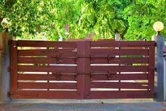 a wooden gate with metal posts in front of some trees and bushes on the sidewalk