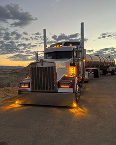 a semi truck is parked on the side of the road at dusk with its lights on