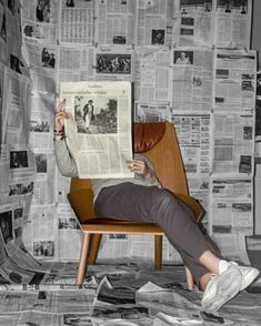 a woman sitting in a chair reading a newspaper while holding her hand up to the side