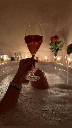 a person holding a wine glass in a hot tub filled with water and lit candles