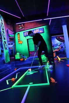 a man is playing mini golf in an indoor setting with neon lights on the floor