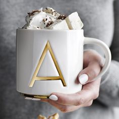 a woman holding a coffee mug with marshmallows and whipped cream in it