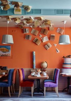 the interior of a restaurant with orange walls and colorful chairs, books falling from the ceiling