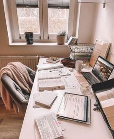 a desk with several books and laptops sitting on top of it next to a window